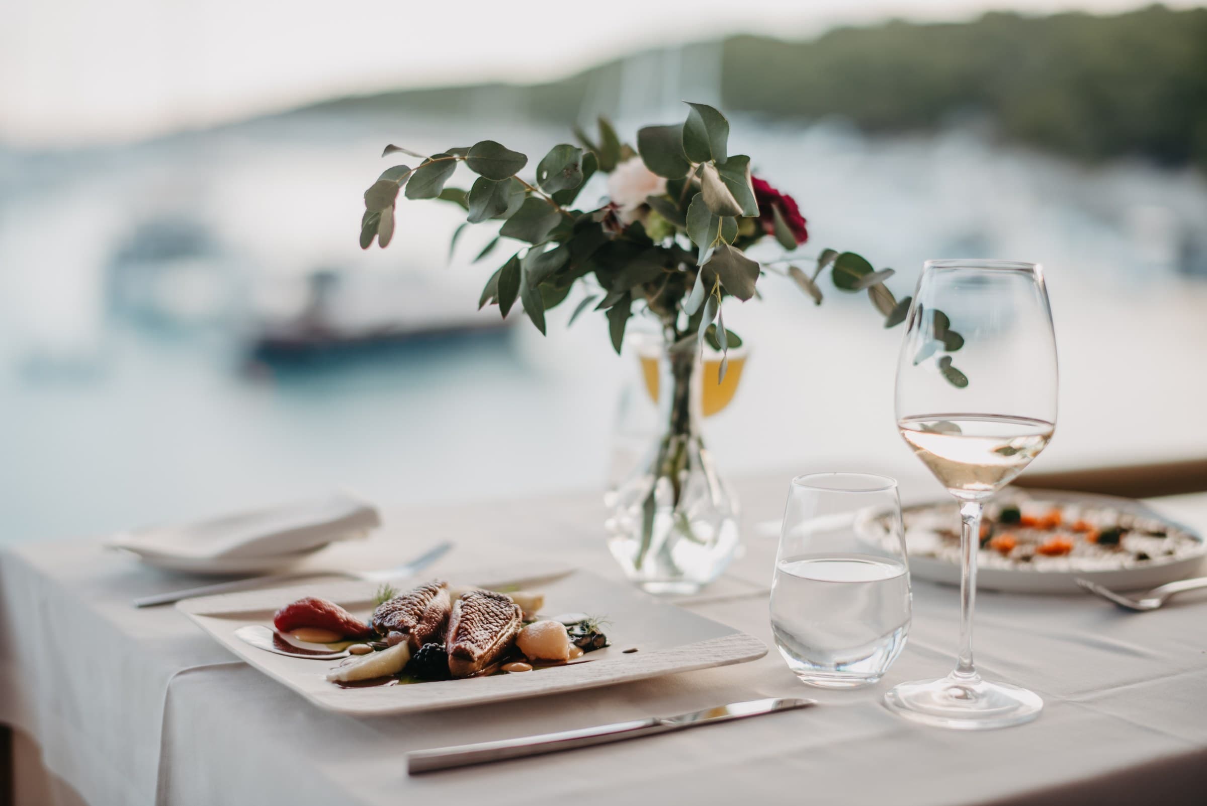 Daily catch plated at the table's edge, the boats of Vinogradišće bay behind it, Zori Restaurant, Palmižana